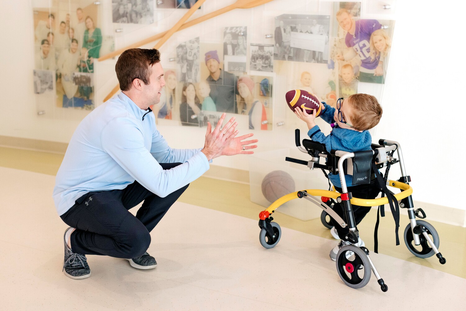 4-year-old Michael Borg, in a walker, passes a football to his dad, Brian Borg, squatting next to him