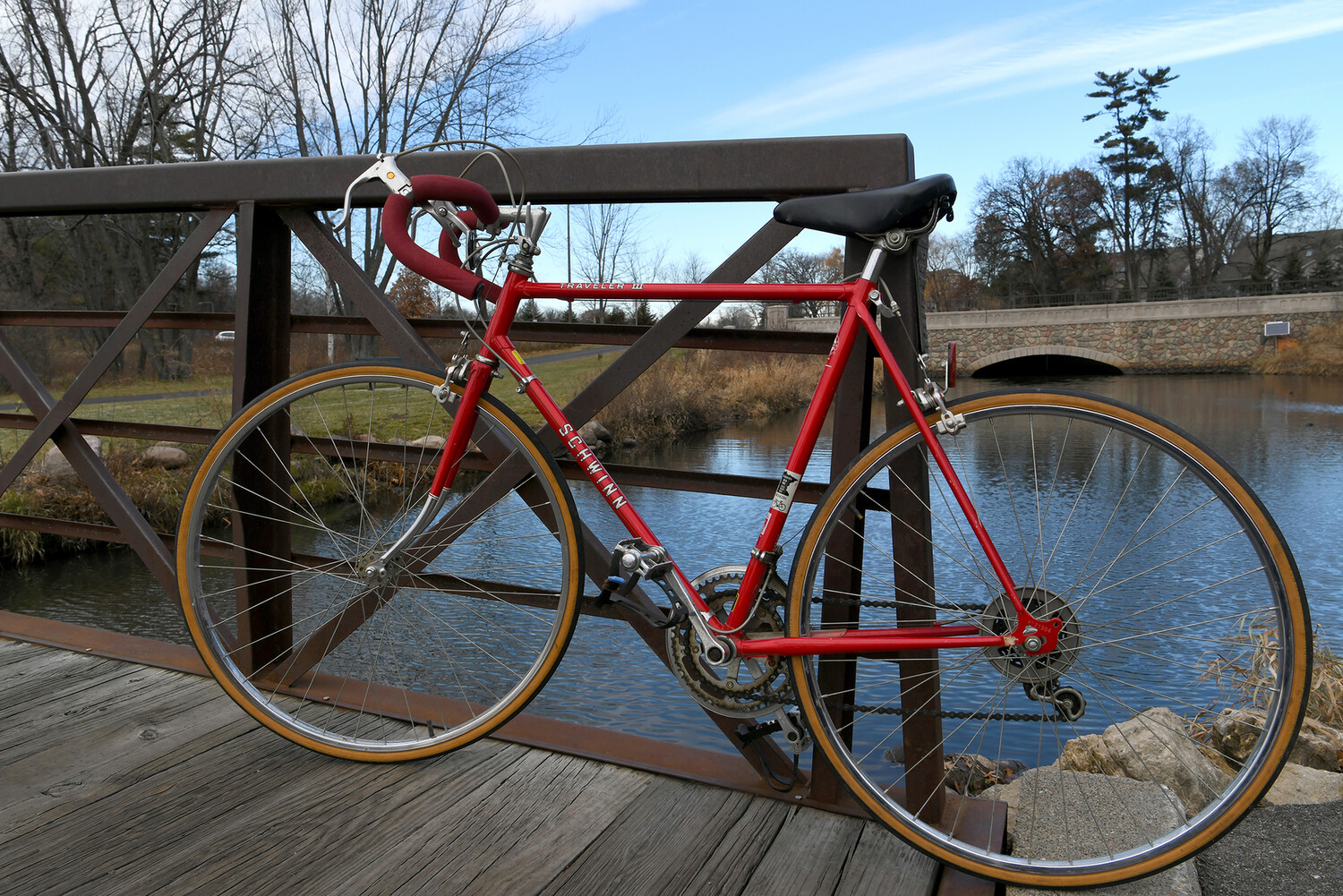 a red 10-speed bike propped up against a railing over a stream on a park trail