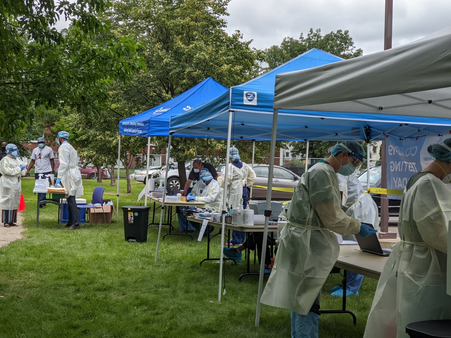 Volunteers in medical gowns and masks work at an outdoor health clinic