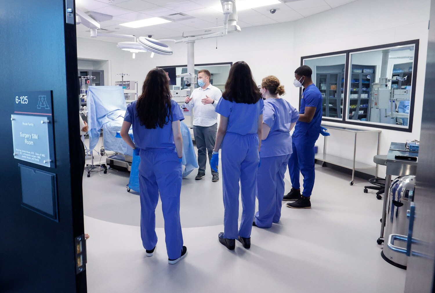 four medical students stand in a mock operating room and listen to an instructor 