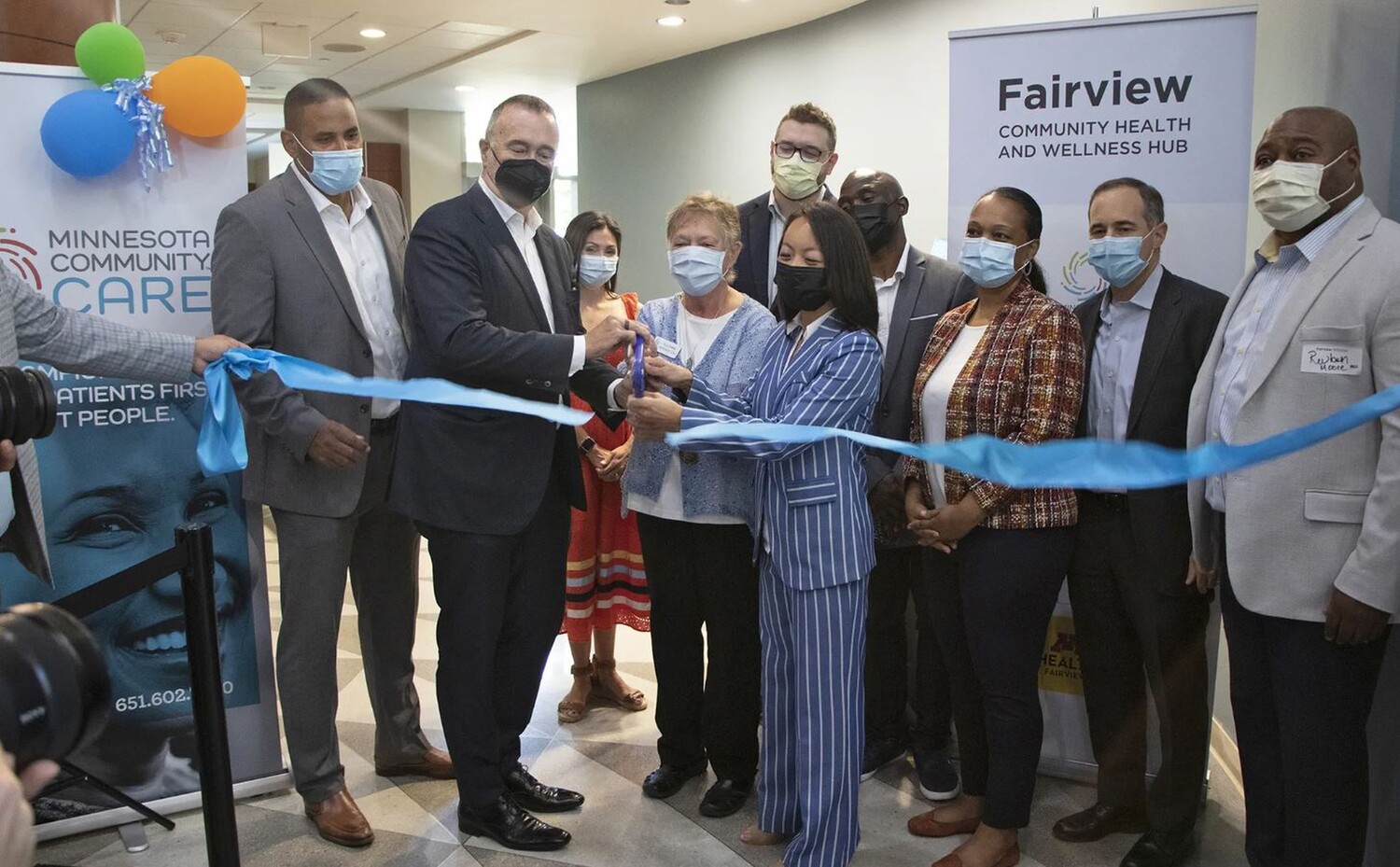 a diverse group of people cut a ceremonial ribbon at the opening of the Fairview Community Health and Wellness Hub